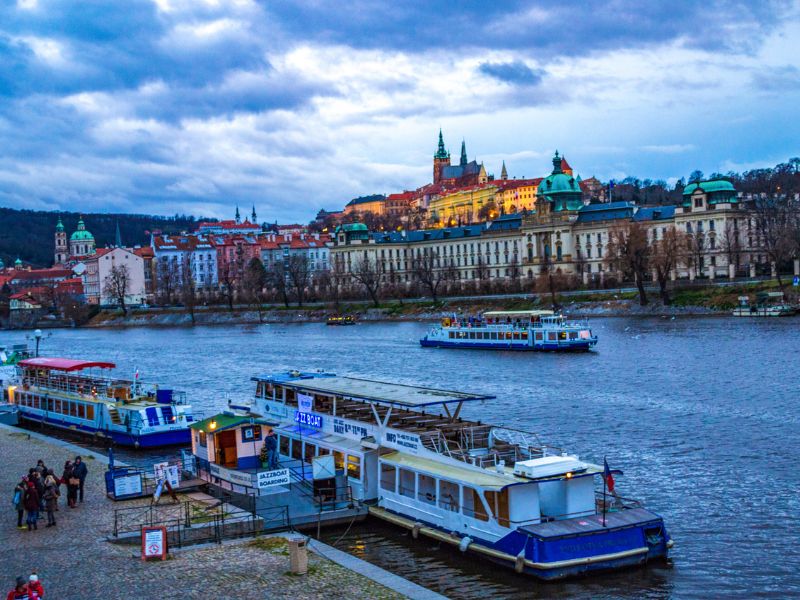 Fluss Moldau im Abendlicht mit Prager Burg im Hintergrund und Schiff